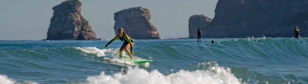 Surfeuse qui prend une vague avec les 2 Jumeaux, les rochers emblématiues d'Hendaye, en fond